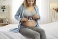 Happy young pregnant woman shows ultrasound scan of baby fetus growing in her belly Royalty Free Stock Photo