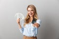 Happy young pretty blonde business woman posing isolated grey wall background holding credit card and money