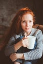 Happy young readhead woman drinking hot coffee or tea at home