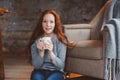 Happy young readhead woman drinking hot coffee or tea at home. Calm and cozy weekend in winter Royalty Free Stock Photo