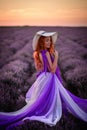 Happy red-haired woman in luxurious dress standing in lavender field at sunset Royalty Free Stock Photo