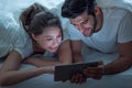 Happy young couple looking a tablet together and laughing while lying on the bed at night Royalty Free Stock Photo