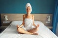 Happy young relaxed woman sitting in yoga pose lotus wrapped bath towel drying her wet hair on bed in the morning Royalty Free Stock Photo