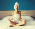 Happy young relaxed woman sitting in yoga pose lotus wrapped bath towel drying her wet hair on bed in the morning Royalty Free Stock Photo