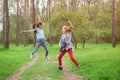 Happy young rock band of two jumping and playing guitar little caucasian girls in green outdoor spring park during rehearsal