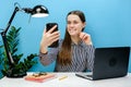 Happy young secretary employee woman in casual shirt sit work at office desk with pc laptop do selfie shot on mobile phone, posing Royalty Free Stock Photo