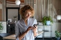 Happy young self employed woman using cellphone alone in office