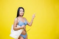 Happy young sexy woman slim body wearing in blue swimsuit holding big shopper bag and sunglasses after shopping pointing finger on Royalty Free Stock Photo