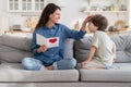 Happy single mom touch kid hair tankful for gift, mum sit on sofa with small son hold greeting card