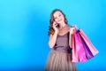 Happy young smiling woman in dress holding shopping bags and talking on mobile smart phone over blue background. Royalty Free Stock Photo