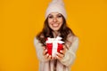 Happy young smiling woman holding and holding red gift box in front, offering and giving Christmas gifts. A girl in a sweater