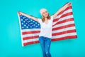 Happy young smiling woman in jeans and white Tshirt wrapped in an American flag, making peace sign and looking at camera. Royalty Free Stock Photo