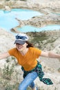 Happy young smiling woman traveler in cap, ginger T-shirt and plaid shirt running on sand of clay quarry with blue turquoise water Royalty Free Stock Photo