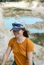 Happy young smiling woman traveler in cap, ginger T-shirt and plaid shirt running on sand of clay quarry with blue turquoise water Royalty Free Stock Photo