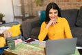 Happy young spanish lady planning summer vacation with map and laptop, choosing best travel routes for future trip