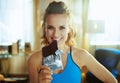 Happy young sports woman in modern house biting chocolate bar Royalty Free Stock Photo