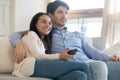 Happy young spouses cuddling on couch at home watching tv