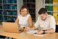 Happy young students of boy and girl preparing in library for exam in university. Two people study. Back view of books Royalty Free Stock Photo