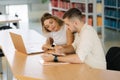 Happy young students of boy and girl preparing in library for exam in university. Two people study. Back view of books Royalty Free Stock Photo