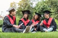 Happy young students relaxing on lawn in graduation clothes Royalty Free Stock Photo