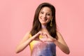 Young stylish disco girl showing heart gesture on pink