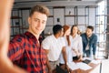 Happy young successful team of multi-ethnic businesspeople making selfie photo in coworking space and smiling looking at Royalty Free Stock Photo