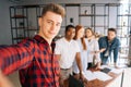 Happy young successful team of multi-ethnic businesspeople making selfie photo in coworking space and smiling looking at Royalty Free Stock Photo