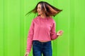 Happy young teenage girl smiling and dancing with blowing hair, wearing pink hoodie and blue jeans. Outdoor image of beautiful Royalty Free Stock Photo