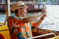 Happy young tourist man taking picture with phone while riding boat on the river