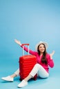 Happy young tourist woman sitting at the suitcase, hugging it and going to travel on holidays isolated on blue background Royalty Free Stock Photo