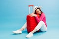 Happy young tourist woman sitting at the suitcase, hugging it and going to travel on holidays isolated on blue background Royalty Free Stock Photo