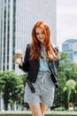 Happy young trendy red hair woman drinking take away coffee and walking in an urban city. Royalty Free Stock Photo