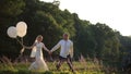 Happy young wedding couple walking with ballooons on the summer field in sunset. Romantic wedding concept