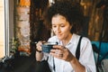 Happy young woman with afro hair drinking hot coffee in modern city cafe. Closeup portrait Royalty Free Stock Photo