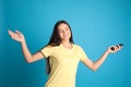 Happy young woman with air conditioner remote control on blue background Royalty Free Stock Photo