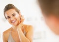 Happy young woman applying cream in bathroom