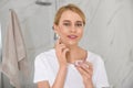 Happy young woman applying cream onto face in bathroom Royalty Free Stock Photo