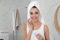 Happy young woman applying cream onto face in bathroom Royalty Free Stock Photo