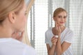 Happy young woman applying cream onto face near mirror in bathroom Royalty Free Stock Photo