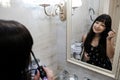 Happy young woman applying mascara in front of a mirror. Girl getting ready with her makeup in a hotel bathroom. Pretty female Royalty Free Stock Photo