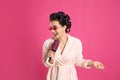 Happy young woman in bathrobe with hair curlers and sunglasses singing into hairbrush on pink background Royalty Free Stock Photo