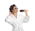 Happy young woman in bathrobe with hair curlers and sunglasses singing into hairbrush on white background Royalty Free Stock Photo