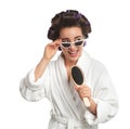 Happy young woman in bathrobe with hair curlers and sunglasses singing into hairbrush on white background Royalty Free Stock Photo