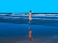 Happy young woman with a beautiful body jumping waves with self reflected on water on beach shore Royalty Free Stock Photo