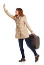 Happy Young Woman In Beige Coat Is Standing With Suitcase, Holding Arm Raised And Waving Royalty Free Stock Photo