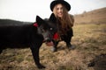 Happy young woman with black hat, plaing with her black dog on the shore of the lake