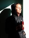 Happy young woman in black raincoat against wall basking in sun autumn day. Smiling girl drinking tea thermo can bottle Royalty Free Stock Photo