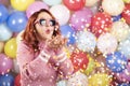 Happy young woman blowing confetti. Redheaded girl party alone on colorful balloons background Royalty Free Stock Photo