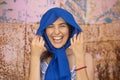 happy young woman with blue headscarf standing in front metal background