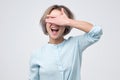 Happy young woman in blue shirt covering her eyes over gray background Royalty Free Stock Photo